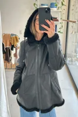 Campera de napalán de cuero genuino color negro, con capucha, cierre frontal, bolsillos laterales y detalles de piel sintética en capucha, puños y ruedo.