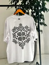 Remera oversize blanca con gran estampado en la espalda de diseño floral simétrico en tono oscuro. Cuenta con mangas cortas y calce holgado.