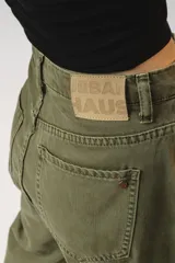 Pantalón de jean color verde oliva, de corte holgado y tiro alto, con pinzas en la cintura y bolsillos laterales.