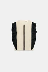 Blusa de cuello redondo y manga sisa, de color beige con rayas verticales. Presenta volantes negros en las sisas y una tira de encaje central con jaretas. Cuenta con cierre en la espalda con abertura y botón.