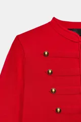 Chaquetas de cuello redondo y manga larga, de color rojo. Cuenta con detalle de botones dorados frontales y en los puños, con cierre delantero con corchetes ocultos.
