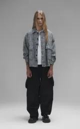 Campera de denim rígido con diseño de trama texturizada en tonos grises y negros. Presenta cuello camisero, cierre frontal con botones, mangas largas y dos bolsillos frontales con solapa.