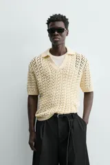 Polo de punto con estructura calada en color beige, confeccionado en algodón. Presenta un calce relajado, manga corta, cuello solapa con abertura frontal y terminaciones acanaladas.