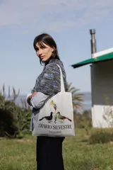 Bolsa tipo tote bag de color blanco, con asas largas para el hombro y estampa frontal con la leyenda 'DIARIO SILVESTRE' acompañada de ilustraciones de aves y flores.