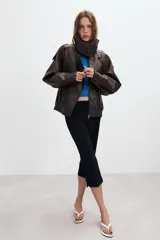 Cazadora tipo biker de cuero sintético en color marrón oscuro, con cuello subido, cierre frontal cruzado con botones forrados y cremallera oculta. Presenta mangas largas con trabillas en los hombros, bolsillos laterales de vivo y bajo con acabado elástico.