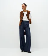 Pantalón wide leg de tiro alto en denim azul oscuro, con cierre frontal de botón y cremallera, bolsillos laterales y cinturón de lazo ajustable confeccionado en la misma tela.