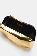 Bolso tipo clutch rígido con acabado metálico dorado y diseño de superficie irregular. Cuenta con cierre superior tipo clip y cadena metálica extraíble para usar como bandolera.