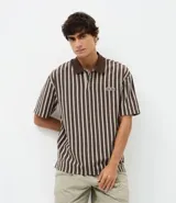 Remera de algodón con diseño rayado en tonos marrones, cuello polo en color sólido y cierre frontal con botones. Presenta un pequeño parche bordado con la palabra 'wave' en el pecho.