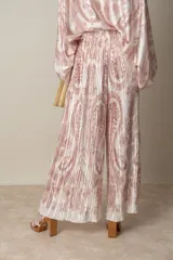 Pantalon palazzo de corte amplio y fluido, confeccionado en tela plisada con estampado estilo paisley en tonos beige y rosado. Presenta cintura elastizada y un diseño ligero ideal para climas cálidos.