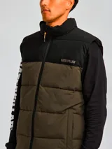 Chaleco acolchado bicolor con diseño de bloques en negro y verde oliva. Presenta cierre frontal completo, cuello alto, bolsillos laterales con cierre y logo de la marca estampado en el pecho.