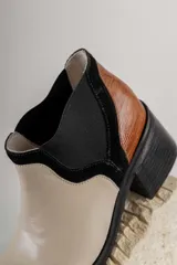 Bota corta de cuero sintético negro con elástico lateral y detalle de estampado animal print en el talón.