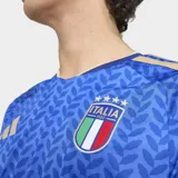 Camiseta de fútbol Adidas de manga corta para hombre, color azul con patrón geométrico en tono más oscuro. Presenta cuello en V con ribete dorado y detalles en los hombros con las tres franjas de Adidas en dorado. Incluye el escudo de la FIGC (Italia) en el pecho izquierdo y el logo de Adidas en el derecho.