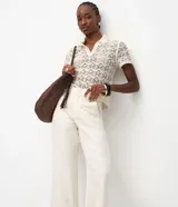 Pantalón de mujer color blanco roto, de corte recto y tiro alto, con un largo cropped y ligero ensanchamiento en el bajo. Presenta detalles bordados florales sutiles en la tela y bolsillos.