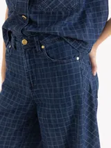 Pantalón wide leg de tiro medio-alto, confeccionado en denim de algodón azul con patrón de cuadros. Cuenta con recortes laterales que aportan volumen y caída fluida, además de bolsillos delanteros y traseros.