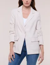 Blazer de silueta semientallada color beige, confeccionado en sastrería liviana de corte fluido, con solapa de muesca clásica, cierre frontal de un solo botón, bolsillos frontales con solapa y mangas largas.