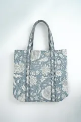 Bolso tipo tote bag acolchado de color celeste y blanco, con estampado floral y asas dobles de hombro decoradas con ribetes trenzados.