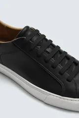 Zapatilla de cordones color negro con parte superior lisa, horma redonda y forro interior a contraste. Suela de goma color crema con ligera textura y detalle en el talón color crema.