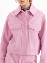 Chaqueta de cuero ovino color negro, con textura graneada, silueta de hombros caídos y largo a la cadera. Presenta recortes en el delantero y la espalda, dos bolsillos superiores con tapa y dos bolsillos laterales, cierre frontal con botones metálicos y cuello camisero.