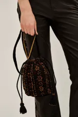 Bolso tipo saco o 'bucket bag' de terciopelo con estampado animal print en tonos marrón oscuro y negro. Presenta costuras verticales en hilo dorado y cordones ajustables negros con borlas y cuentas doradas en los extremos.
