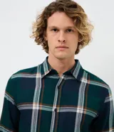 Camisa de manga larga confeccionada en franela de viscosa y poliéster, con estampado de cuadros escoceses en tonos verde, azul y marrón. Presenta cuello clásico y cierre frontal con botones.