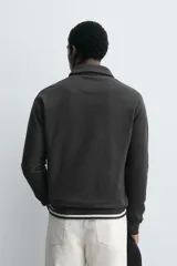 Polo de manga larga color gris oscuro, con diseño de textura estructurada, cuello solapa y cierre frontal de cremallera corta. Cuenta con puños y cintura de rib elástico.