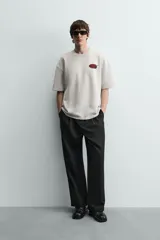 Sudadera gris de corte relaxed fit, cuello redondo y manga corta. Presenta un estampado en el pecho con la frase "Tokyo Kitchen" en un óvalo rojo con palillos.