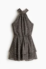 Vestido corto de gasa transparente en color negro con estampado floreado. Presenta escote halter alto, espalda abierta, elástico fruncido en la cintura y falda escalonada con vuelo. Incluye forro interior.