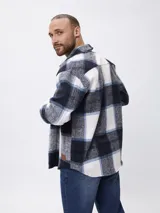 Sobrecamisa de corte recto con estampado de cuadros en tonos azul, blanco y gris. Presenta cuello clásico, cierre frontal con botones, mangas largas con puños abotonados y bolsillos frontales en el pecho.