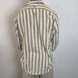 Camisa de lino de corte oversize con diseño de rayas verticales en tonos blanco y tostado, manga larga y cierre frontal con botones.
