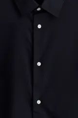 Camisa de tela azul marino con tratamiento de fácil planchado. Modelo Slim Fit con cuello inglés, tapeta clásica, canesú en la espalda, mangas largas con tapeta y botón, y puños ajustables con botón. Bajo ligeramente redondeado.