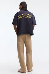 Remera negra de algodón con corte boxy y oversized, cuello redondo y mangas cortas. Cuenta con un pequeño estampado dorado en el pecho con texto y estrellas.