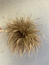 Broche decorativo confeccionado con plumas de avestruz en tono marrón, con estructura circular y volumen.