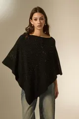 Poncho negro de tejido de punto con diseño asimétrico y detalle de pequeñas aplicaciones brillantes distribuidas por toda la superficie. Presenta un borde acanalado en el ruedo.