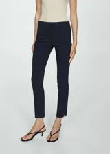 Pantalón de vestir azul marino de corte ajustado y tobillero, con bolsillos laterales, trabillas para cinturón y cierre frontal con cremallera y botón oculto. Presenta pequeñas aberturas en los bajos.