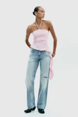 Top negro de cuello halter con lazada, escote recto y hombros descubiertos. Presenta un volante asimétrico en el lateral.