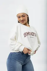 Buzo color crema con estampado frontal que dice "SMOOTH" en marrón y "REDCHARCOAL" debajo. Tiene cuello redondo y mangas largas.