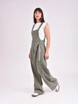 Monoprenda (jardinera) color verde oliva, de corte holgado y pierna ancha, con tirantes ajustables, cierre frontal de botones y lazo para ajustar en la cintura.