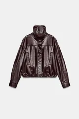Chaqueta de efecto piel en color bordó, con cuello subido, manga larga con puños y cierre frontal con cremallera y botones a presión ocultos. Presenta bolsillos laterales y bajo con elástico.
