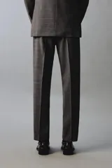 Pantalón de traje de corte regular fit, confeccionado en lana de origen italiano. Presenta un diseño a cuadros sutiles, bolsillos delanteros, bolsillos traseros de doble vivo con botón y cierre frontal con cremallera y botón.