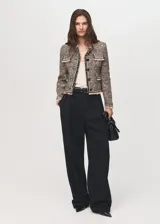 Chaqueta de tweed con diseño recto y cuello redondo. Presenta cierre frontal con botones, manga larga y cuatro bolsillos de solapa en la parte delantera. Destaca por sus terminaciones deshilachadas y ribetes en contraste.