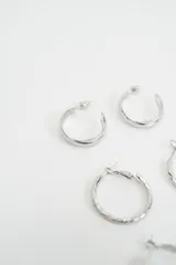 Set de tres pares de aros tipo argolla en color plateado, con diferentes texturas y tamaños, incluyendo un par liso pequeño, un par con textura trenzada mediano y un par liso grande.
