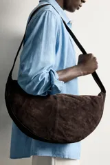 Bolso de hombro de diseño semicircular, confeccionado en piel con acabado serraje de color marrón. Cuenta con una sola asa de hombro y cierre principal con cremallera.