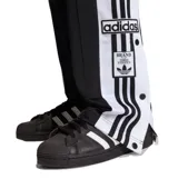 Pantalon deportivo Adidas modelo Adibreak, color negro con franjas laterales blancas y botones a presión. Presenta el logo de la marca y diseño de tres tiras icónico en los costados.
