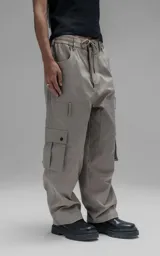 Pantalón cargo de corte oversize y silueta estructurada, confeccionado en microfibra pesada con leve elasticidad. Presenta cintura elástica con cordón de ajuste externo, cierre frontal con botón metálico, bolsillos laterales y bolsillos cargo de gran tamaño con tapa y broches a presión.