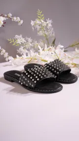 Sandalias chatas negras con tira ancha sobre el empeine, cubierta de tachas plateadas.