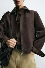 Cazadora cropped fit color marrón oscuro, confeccionada en tejido de algodón. Presenta cuello solapa, manga larga con puño abotonado, bolsillos de vivo en la cadera y un bolsillo interior. El bajo tiene elástico en la espalda y el cierre es frontal con cremallera.