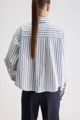 Camisa de calce relajado confeccionada en algodón, con diseño de rayas verticales en tonos beige y blanco. Presenta cuello clásico, cierre frontal con botones, puños abotonados y largo ligeramente cropped.