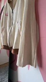 Campera de algodón premium color crudo con detalles en marrón y rosa. Presenta un cierre frontal, cuello redondo, mangas largas acampanadas y un logo bordado en el pecho.