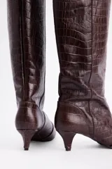 Bota de caña alta confeccionada en cuero vacuno con textura de reptil. Presenta un diseño de punta fina y un tacón bajo tipo kitten heel.