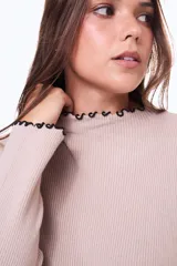 Buzo de tejido de punto acanalado en color beige, con cuello alto y terminaciones con borde ondulado en contraste negro en cuello y puños.